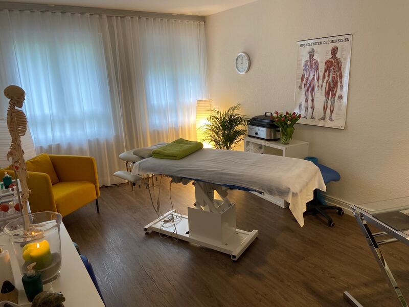 Behandlungsraum mit Therapieliege, gelbem Sessel, Skelettmodell und mehreren Behandlungsutensilien.